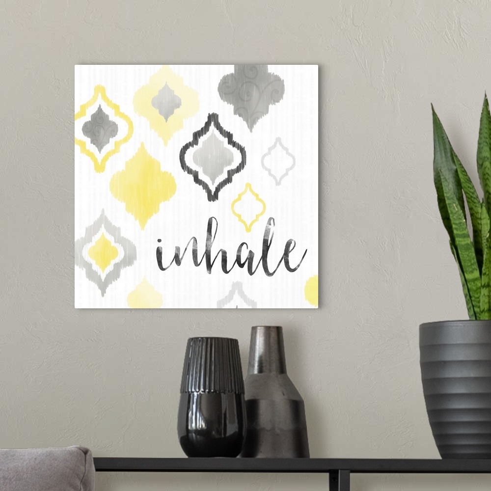 A modern room featuring A square decorative artwork of Moroccan tile designs in yellow and gray with the text 'inhale'.
