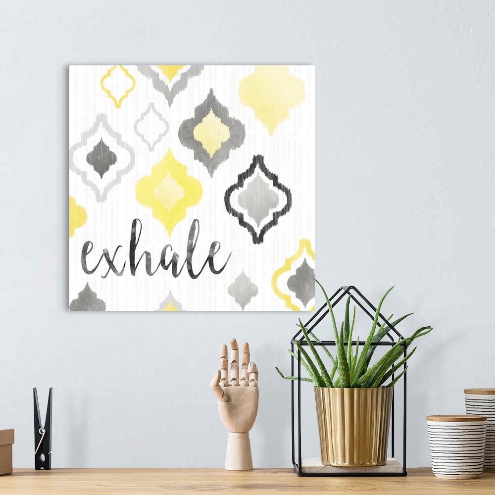 A bohemian room featuring A square decorative artwork of Moroccan tile designs in yellow and gray with the text 'exhale'.