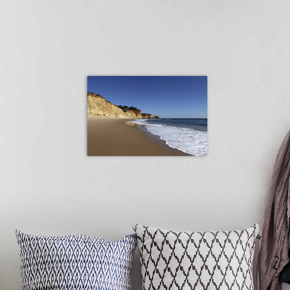 A bohemian room featuring A wave washes an empty beach of golden sand, with steep cliffs, Algarve, Portugal