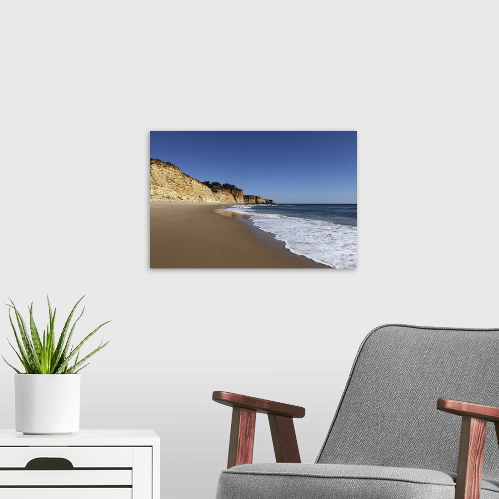 A modern room featuring A wave washes an empty beach of golden sand, with steep cliffs, Algarve, Portugal