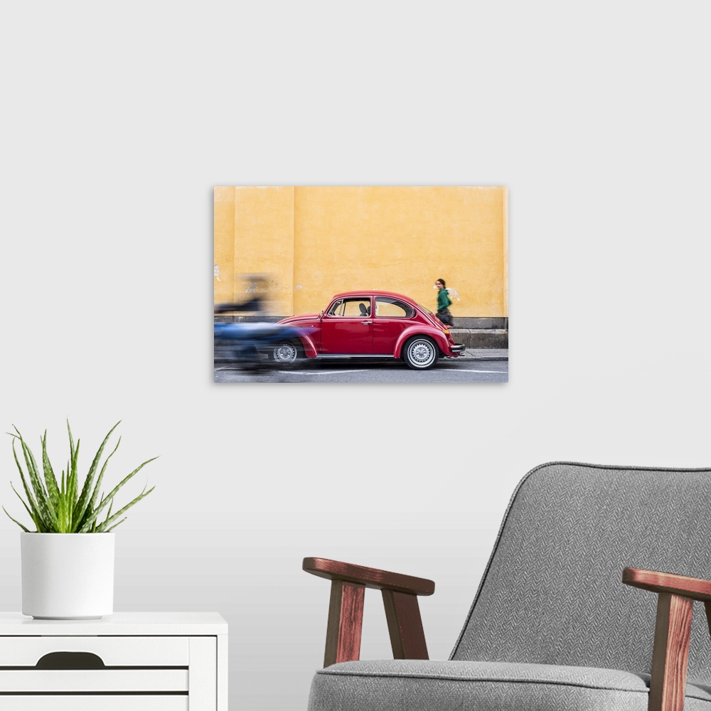 A modern room featuring A woman walking past a red VW Beetle in the colourful streets of Popayan, Colombia, South America