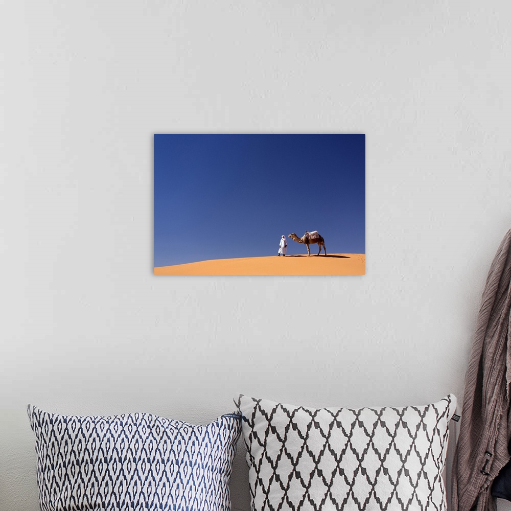 A bohemian room featuring Berber man with camel on the ridge of an orange sand dune in the Erg Chebbi sand sea, Sahara Dese...