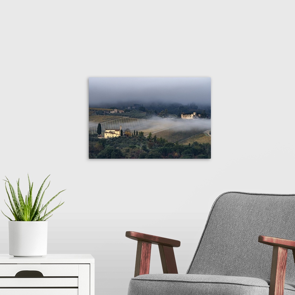 A modern room featuring Castello di Gabbiano across a misty valley, church in foreground, San Casciano, Tuscany, Italy, E...