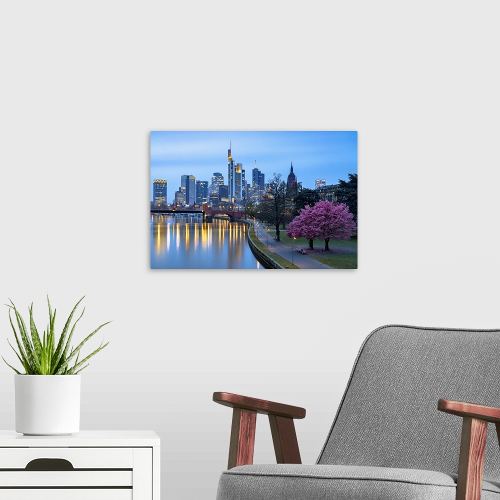 A modern room featuring Cherry tree in bloom on banks of River Main with skyline of business district in the background a...