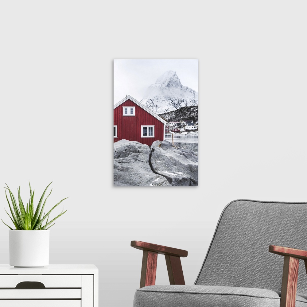 A modern room featuring Red Rorbu in the frozen landscape with snowcapped Olstind mountain in the background, Reine, Nord...