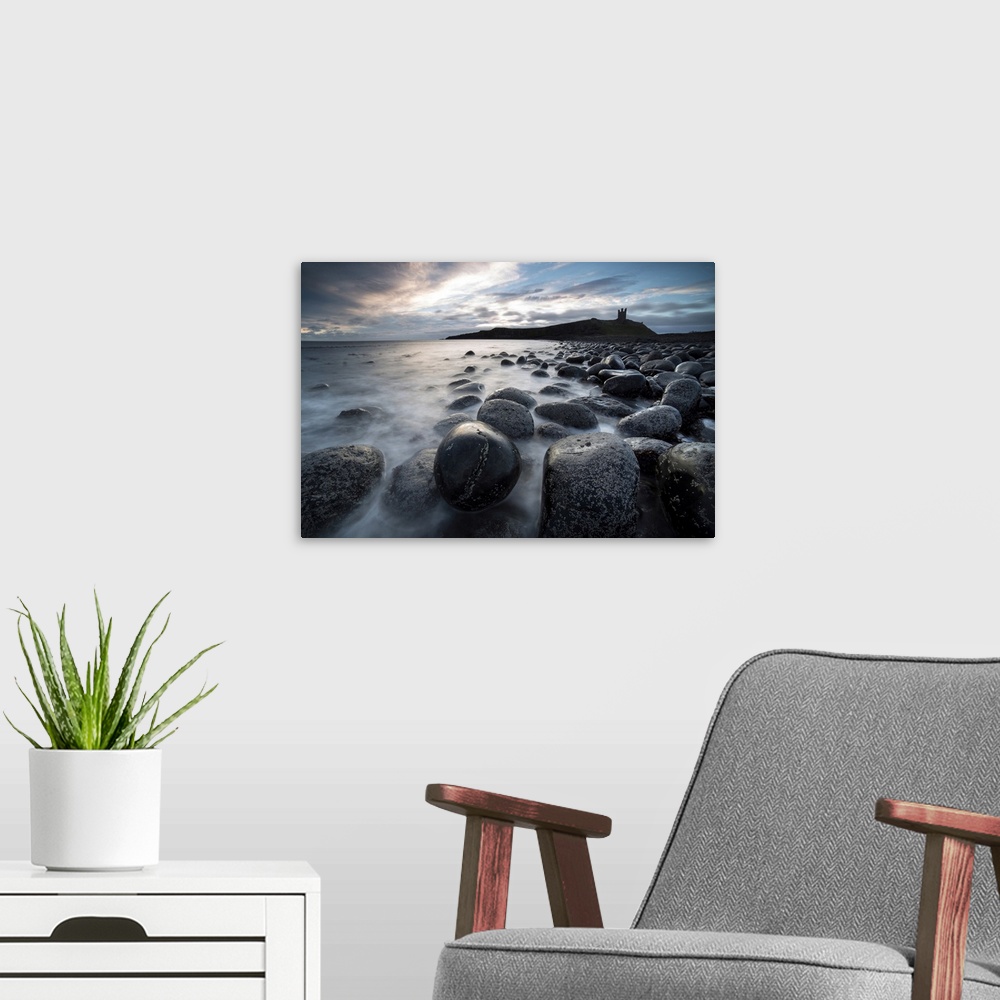 A modern room featuring View at sunrise towards the ruin of Dunstanburgh Castle from the beach of basalt boulders known a...