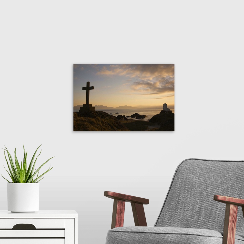 A modern room featuring Stone Cross and old lighthouse in silhouette at sunset, Anglesey, North Wales, UK