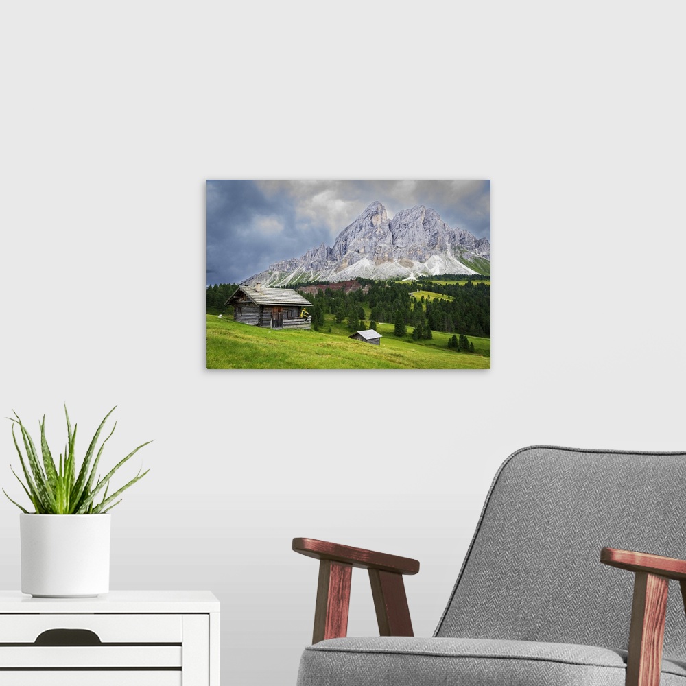 A modern room featuring Side view of a hiker on chalet in green meadows admiring the rocky massif of Sass de Putia, Passo...