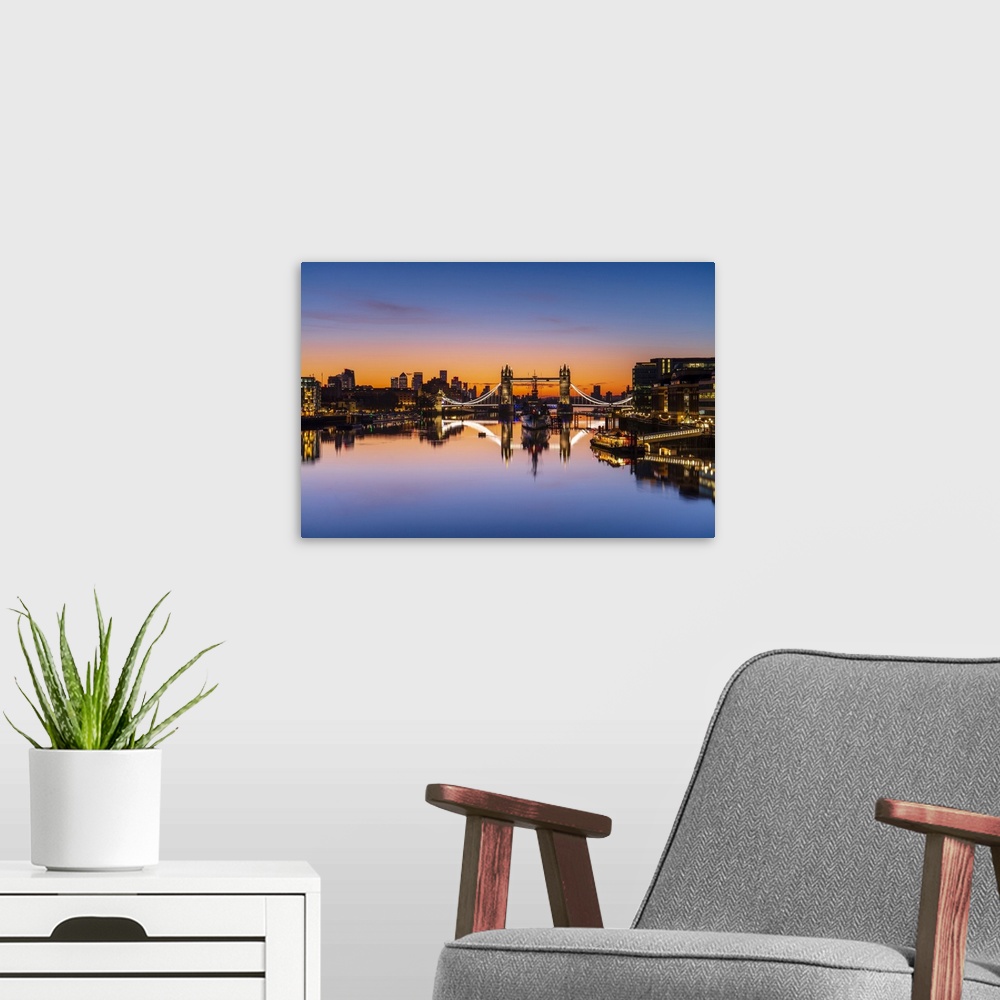 A modern room featuring Tower Bridge, HMS Belfast and reflections in a still River Thames at sunrise, London, England, Un...