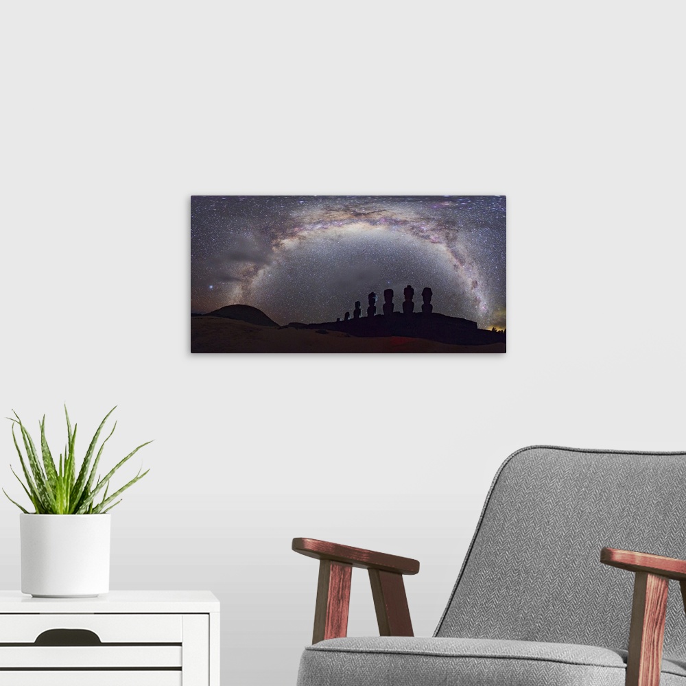 A modern room featuring Easter Island moai and Milky Way. Panoramic view of the arch of the Milky Way in the night sky ov...