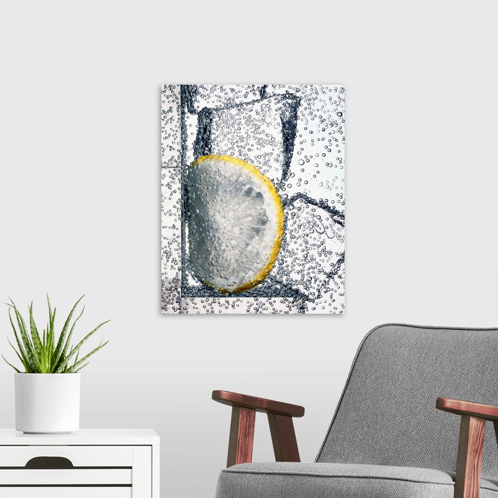 A modern room featuring Lemonade. Bubbles rise from this carbonated water drink which has ice cubes and a slice of lemon ...