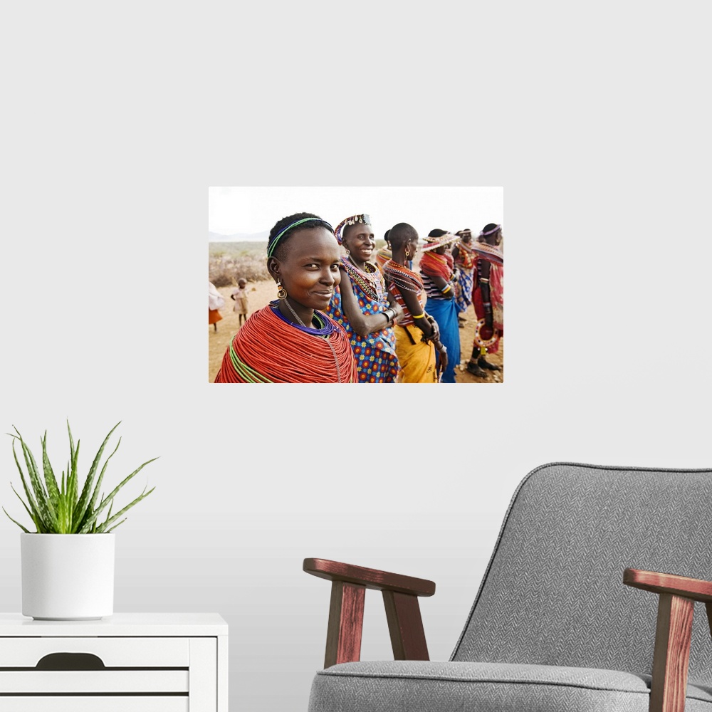 A modern room featuring Oversized landscape photograph of the African Samburu Tribe, forming a line and dressed in bright...