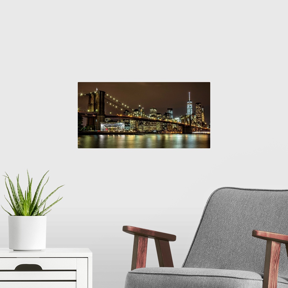 A modern room featuring Panoramic photograph of the Brooklyn Bridge illuminated at night, reflected in the water below, w...