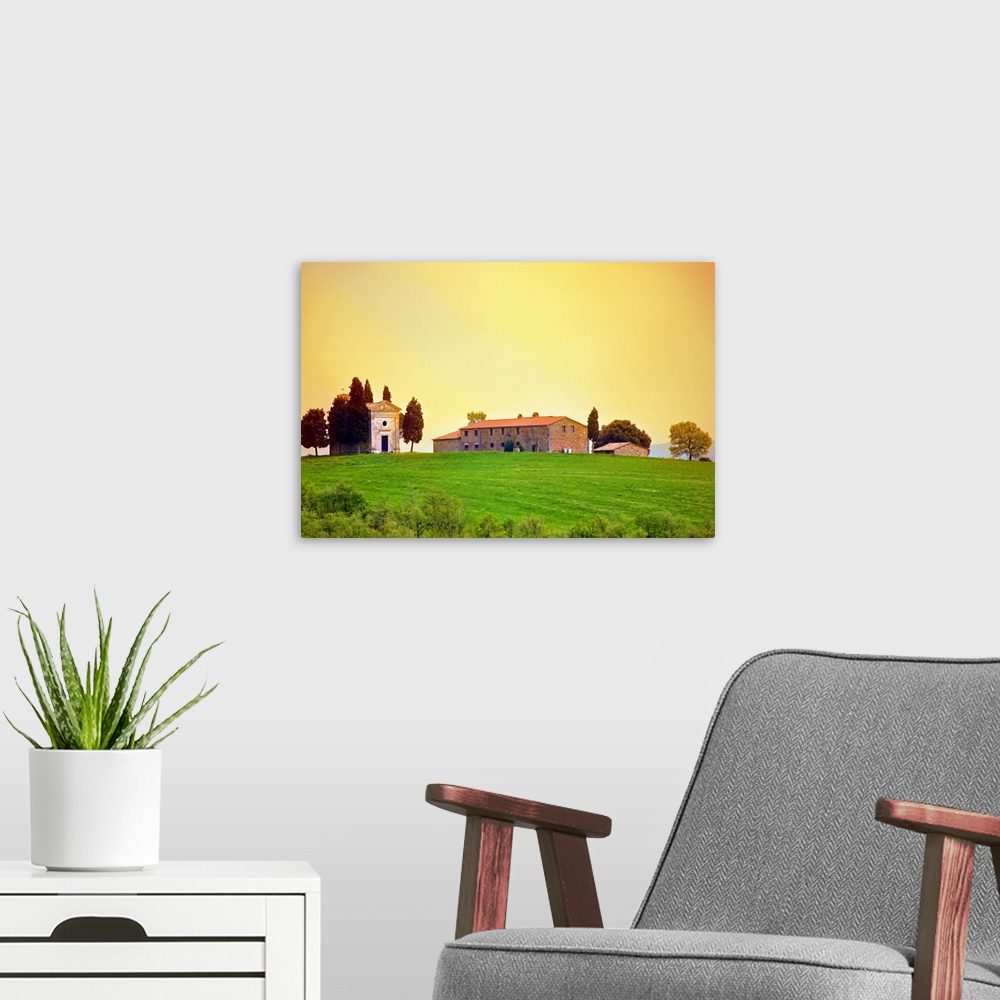 A modern room featuring Old traditional Tuscan farm buildings set on a green grass hill with a clear sunset sky.