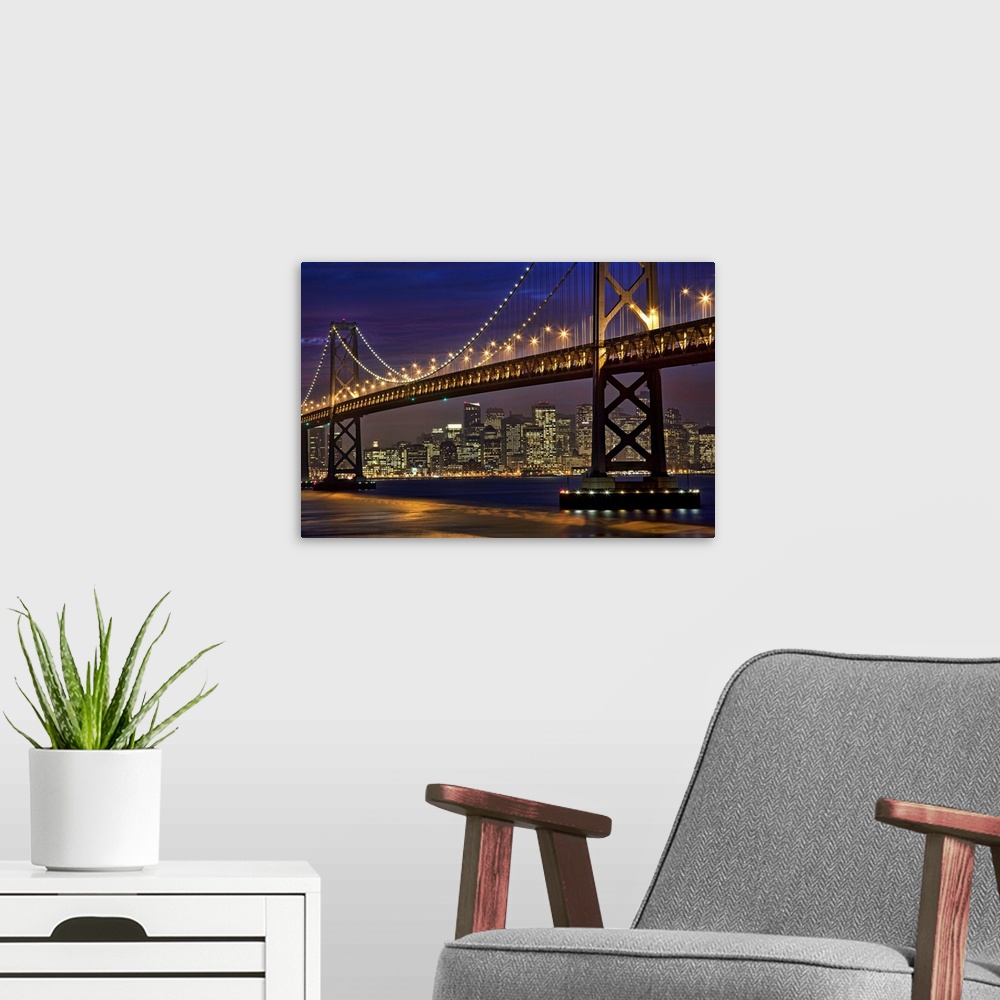 A modern room featuring The Bay Bridge is shining brightly under a night sky with the San Francisco skyline shown in the ...