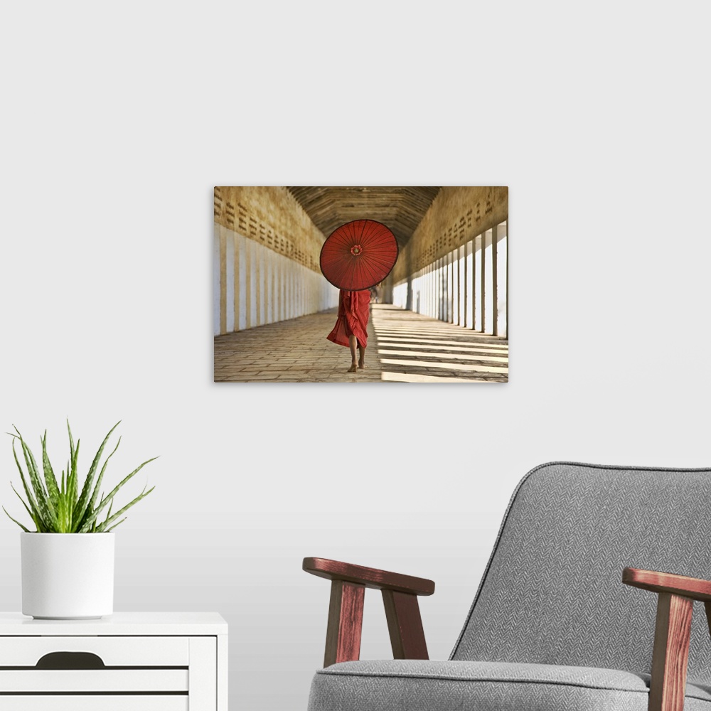A modern room featuring Horizontal photograph of a Monk covered from the shoulders up by an umbrella, walking down the st...