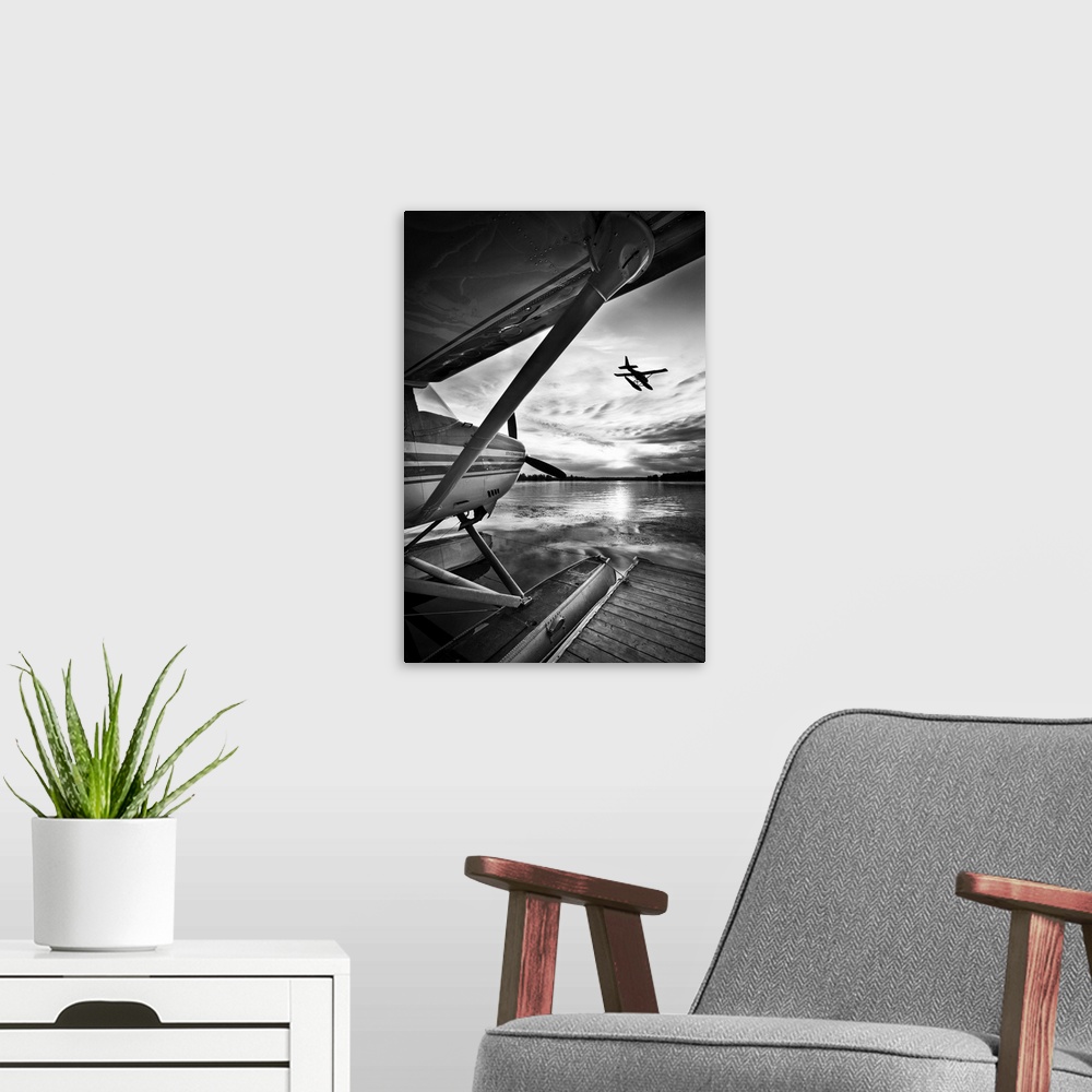 A modern room featuring A black and white photograph taken from under the wing of a plane docked in the water while anoth...