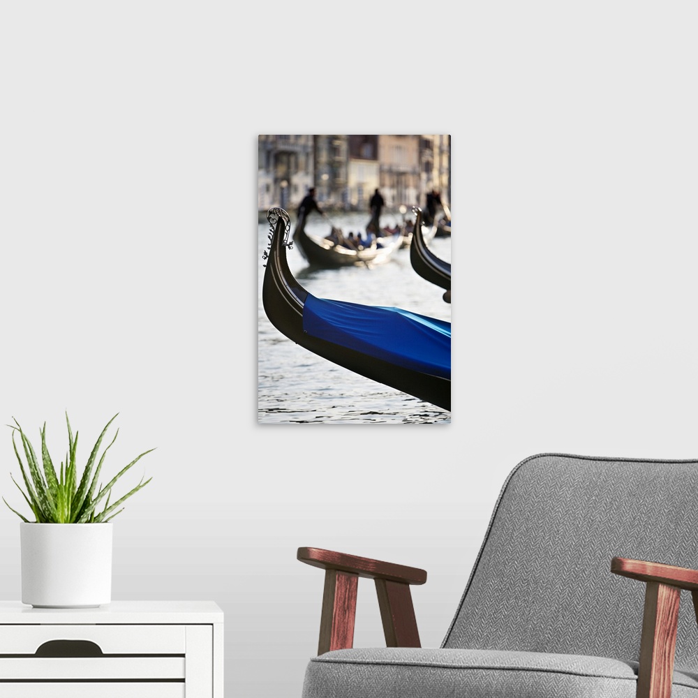 A modern room featuring Vertical photograph of the front tip of a Venetian gondola hanging over the water.  In the backgr...