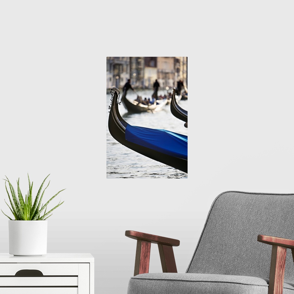 A modern room featuring Vertical photograph of the front tip of a Venetian gondola hanging over the water.  In the backgr...