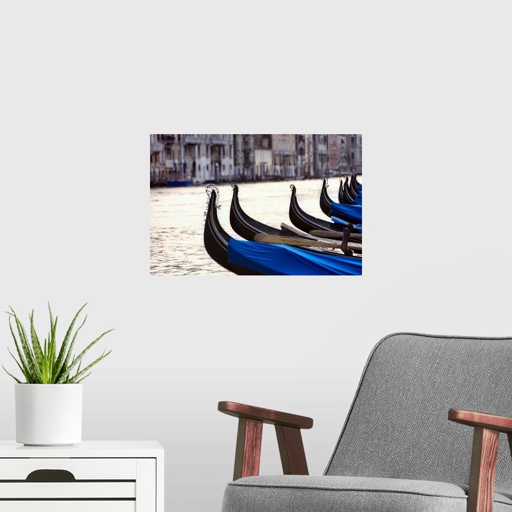 A modern room featuring Horizontal photograph on a big canvas of a row of the front ends of gondolas on the water.  A row...