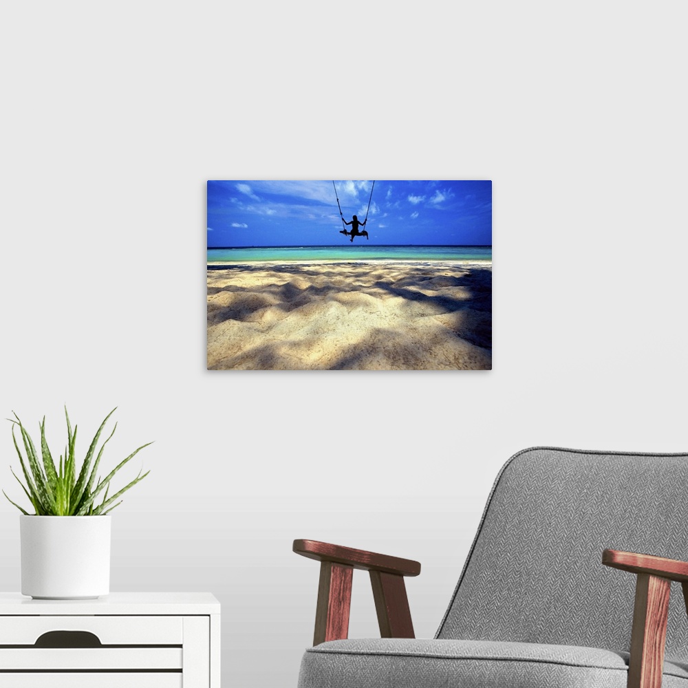 A modern room featuring landscape, large photograph of the silhouette of a woman on a swing over the sandy beach, looking...