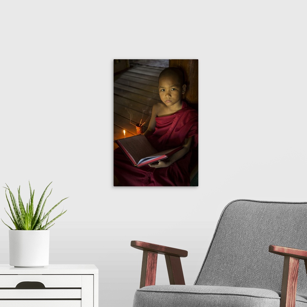 A modern room featuring Young Burmese monk reading by candlelight