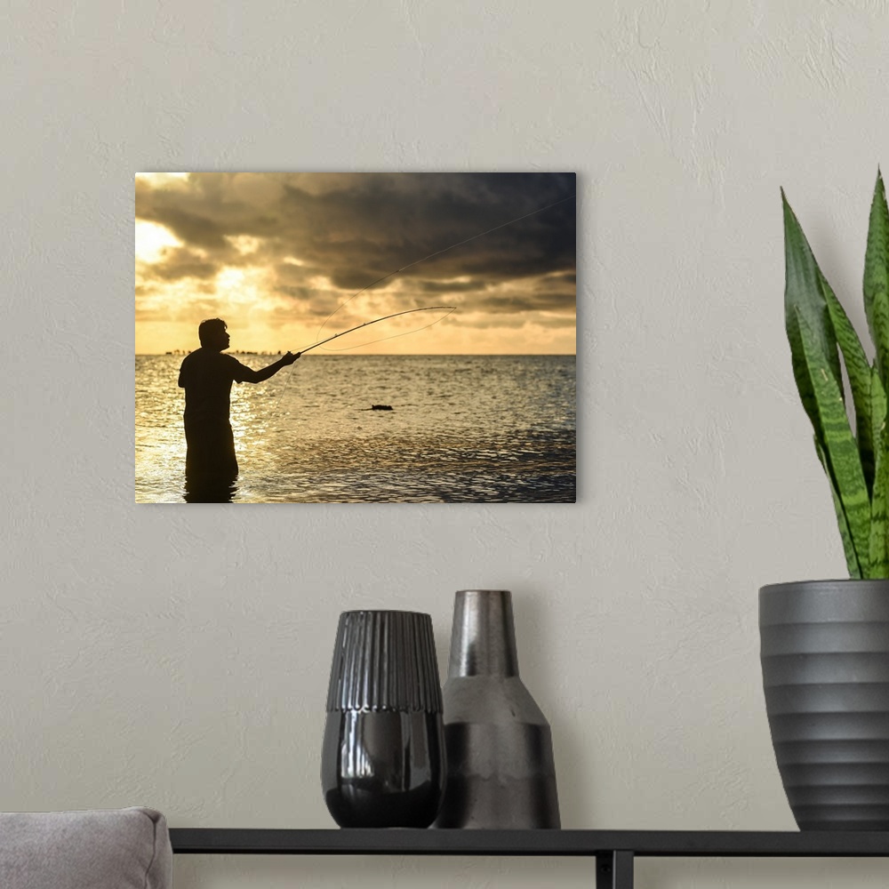A modern room featuring A silhouetted man fly fishing on the beach in Belize at sunset.