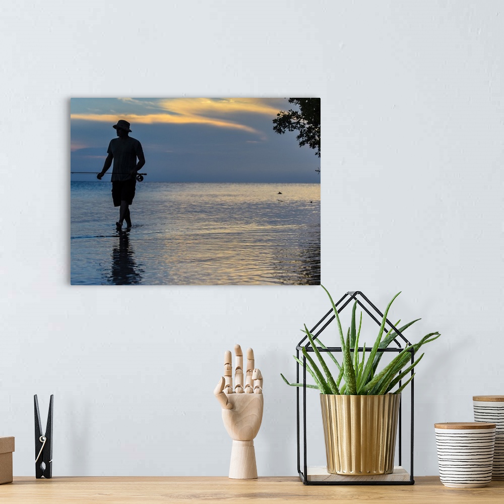 A bohemian room featuring A silhouetted man fly fishing on the beach in Belize at sunset.