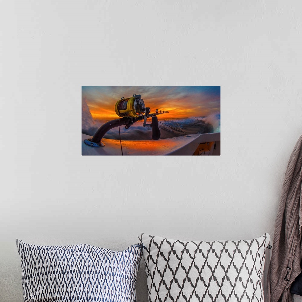 A bohemian room featuring The reel of a big game fishing rod on the side of a boat, with the setting sun behind