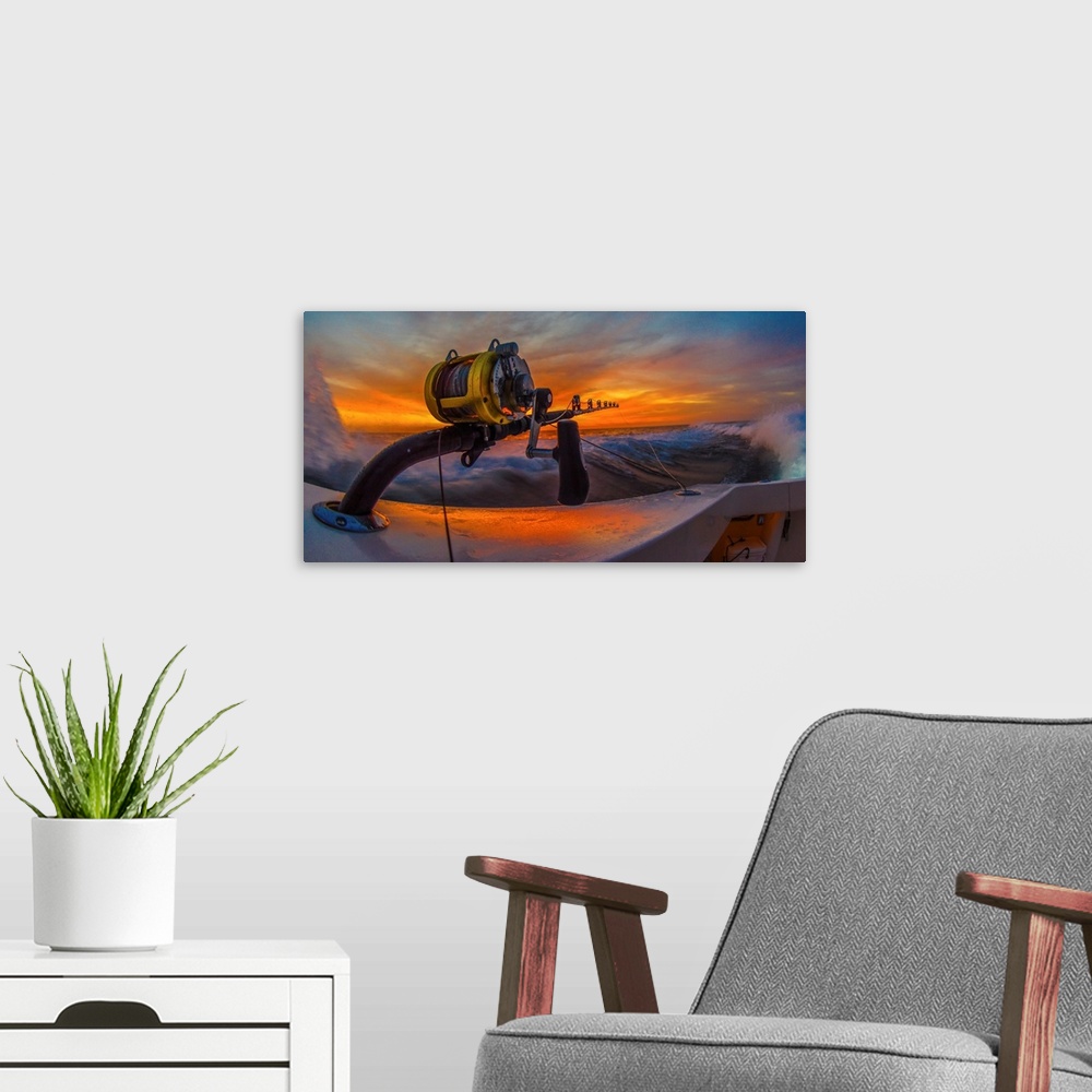 A modern room featuring The reel of a big game fishing rod on the side of a boat, with the setting sun behind