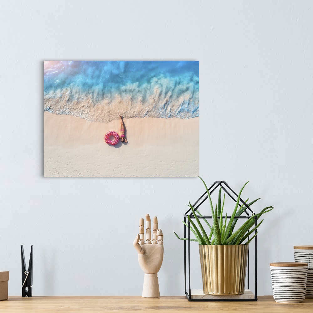 A bohemian room featuring Aerial view of the beautiful young lying woman with pink donut swim ring on the white sandy beach...