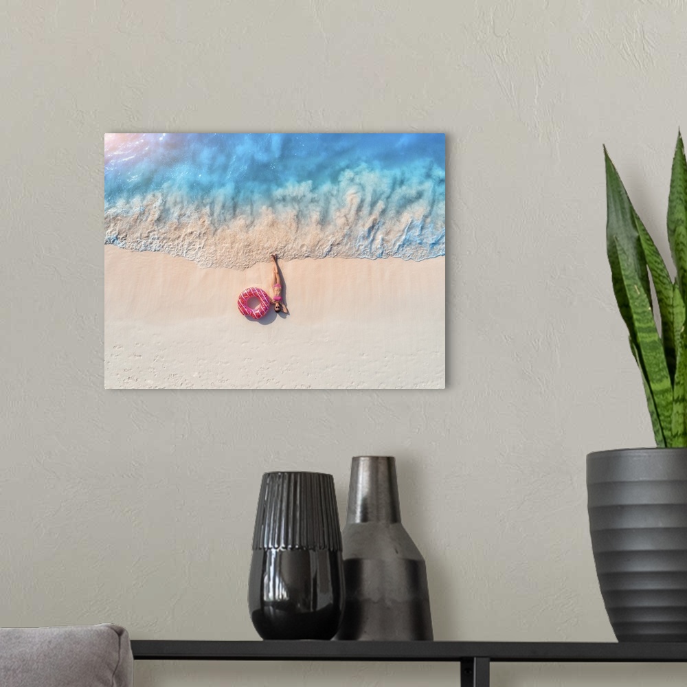 A modern room featuring Aerial view of the beautiful young lying woman with pink donut swim ring on the white sandy beach...