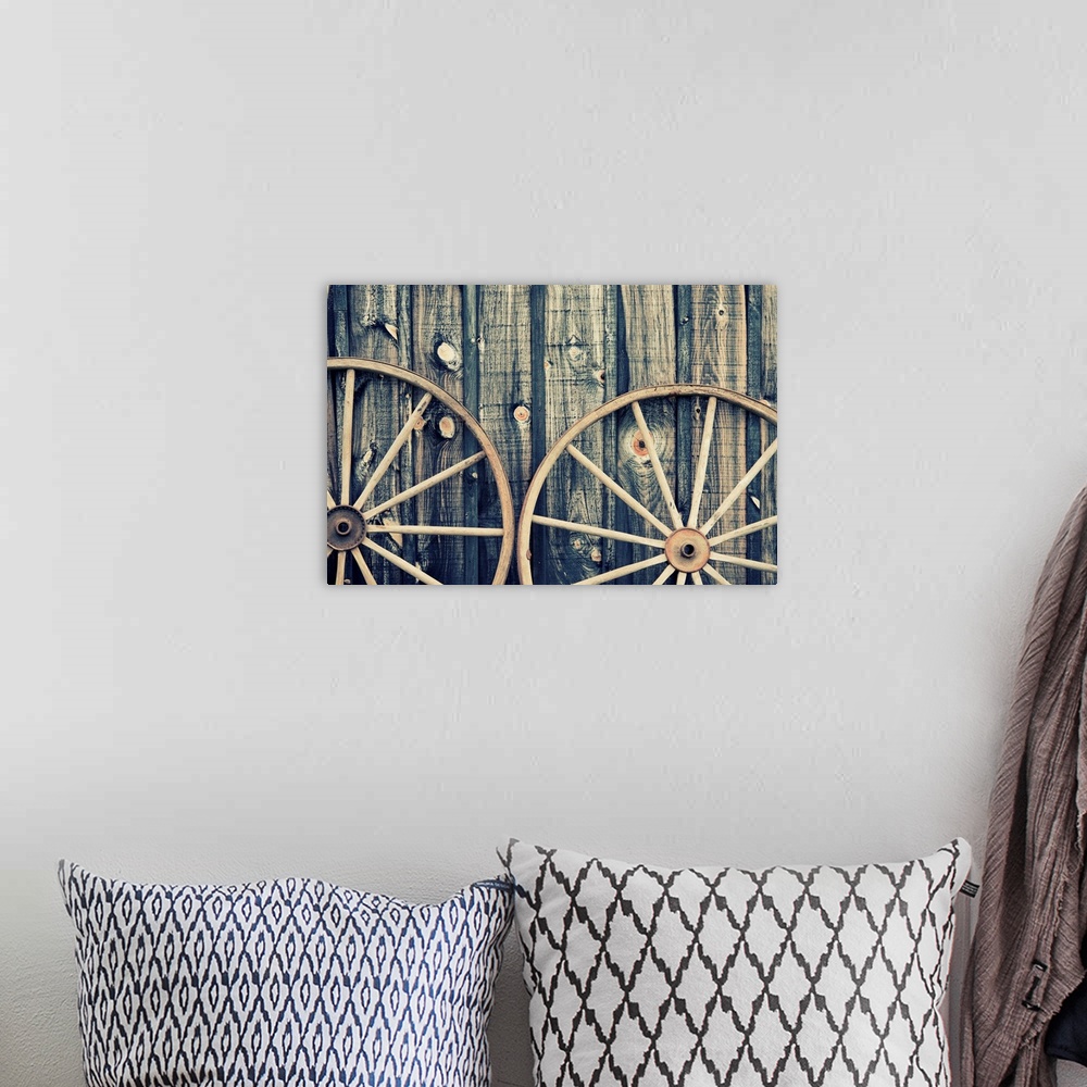 A bohemian room featuring A close up of two vintage wagon wheels lying up against a building.