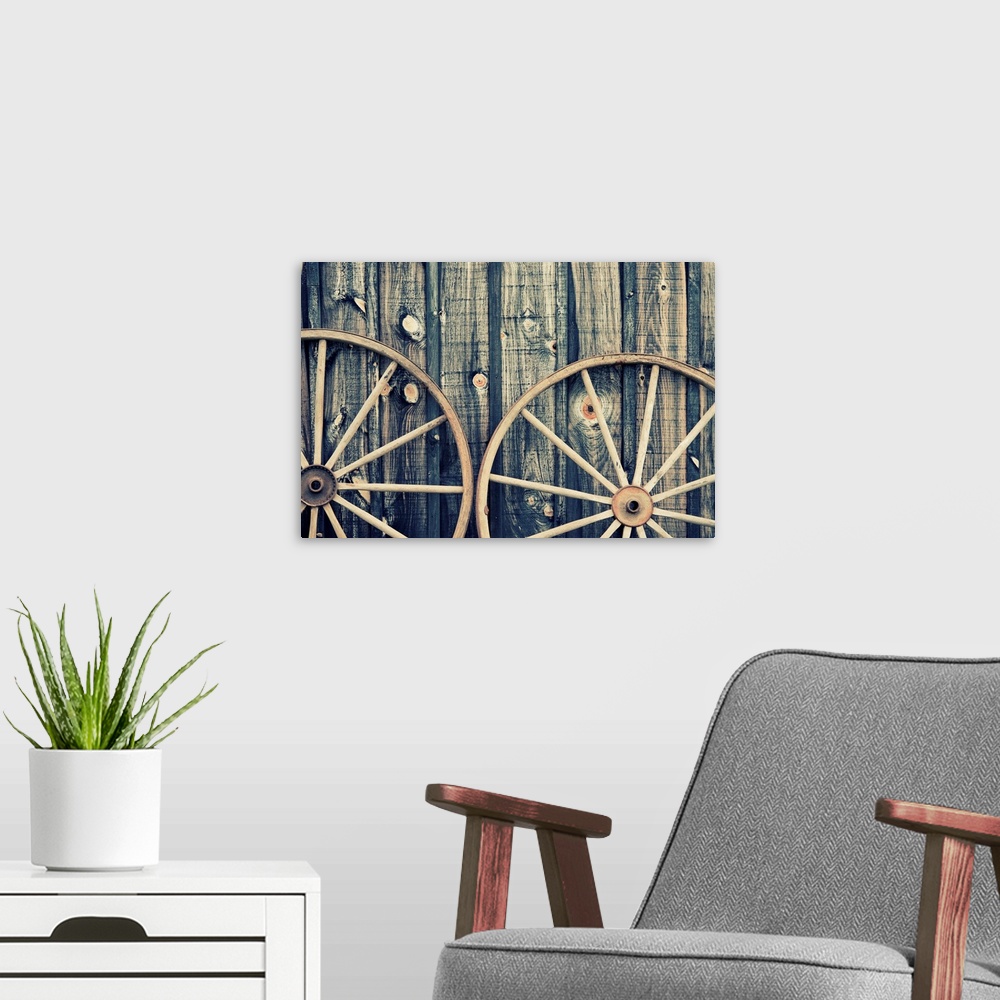 A modern room featuring A close up of two vintage wagon wheels lying up against a building.