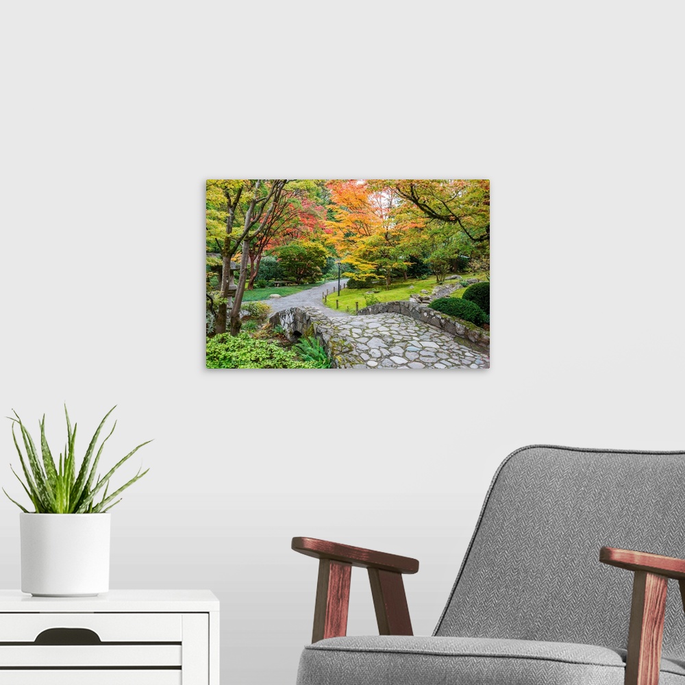 A modern room featuring Autumn colors along a winding walking path and stone bridge in a Japanese garden.