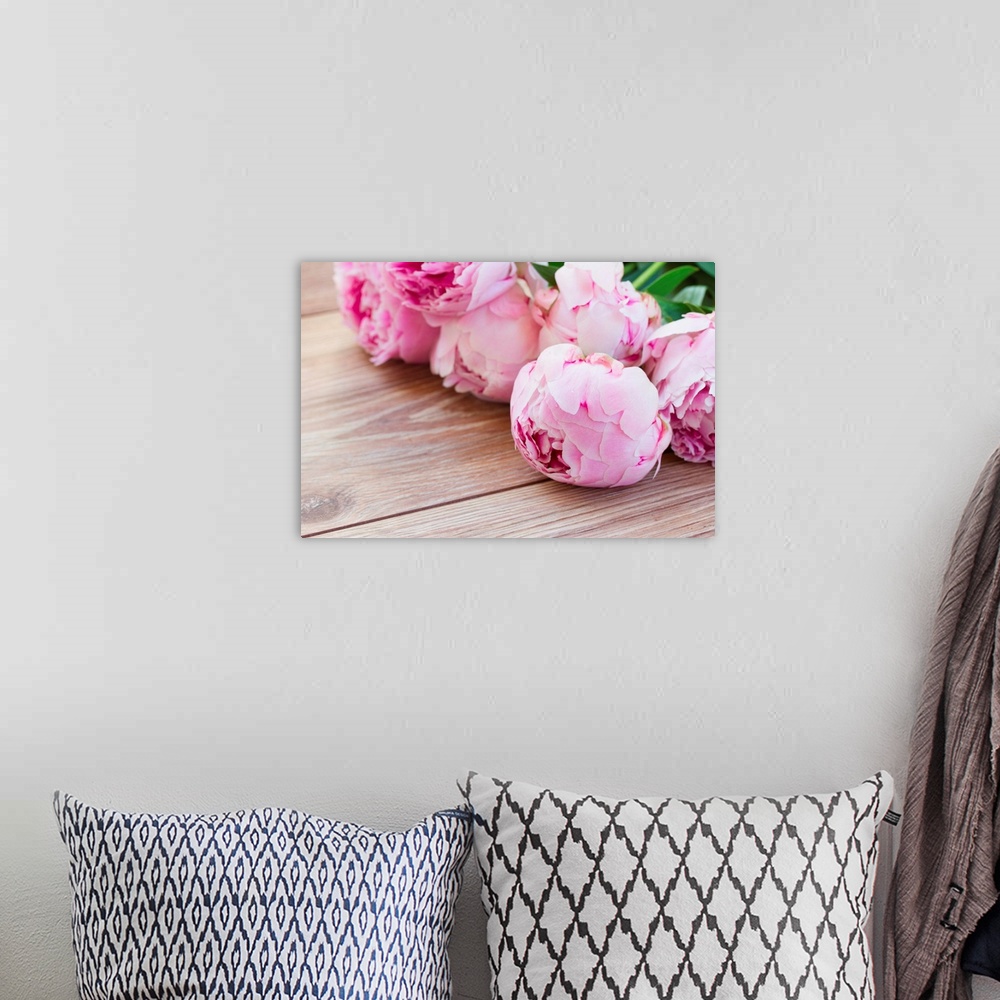A bohemian room featuring Bouquet of pink peonies laying on wooden table.