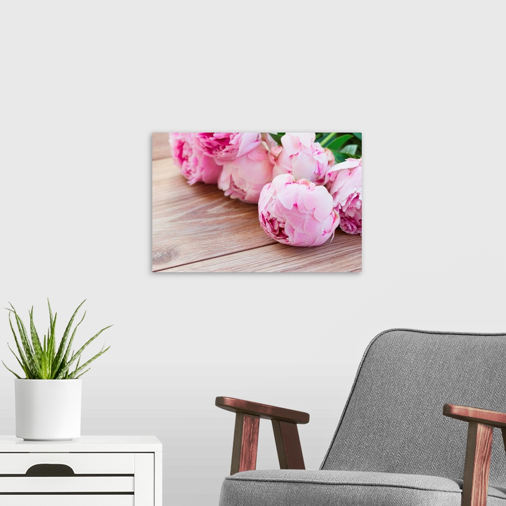 A modern room featuring Bouquet of pink peonies laying on wooden table.