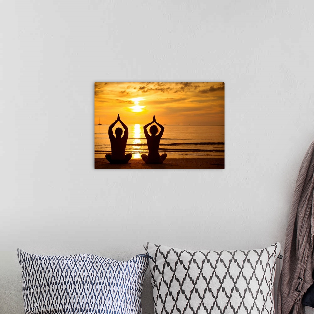 A bohemian room featuring Young couple practicing yoga on the sea beach at sunset