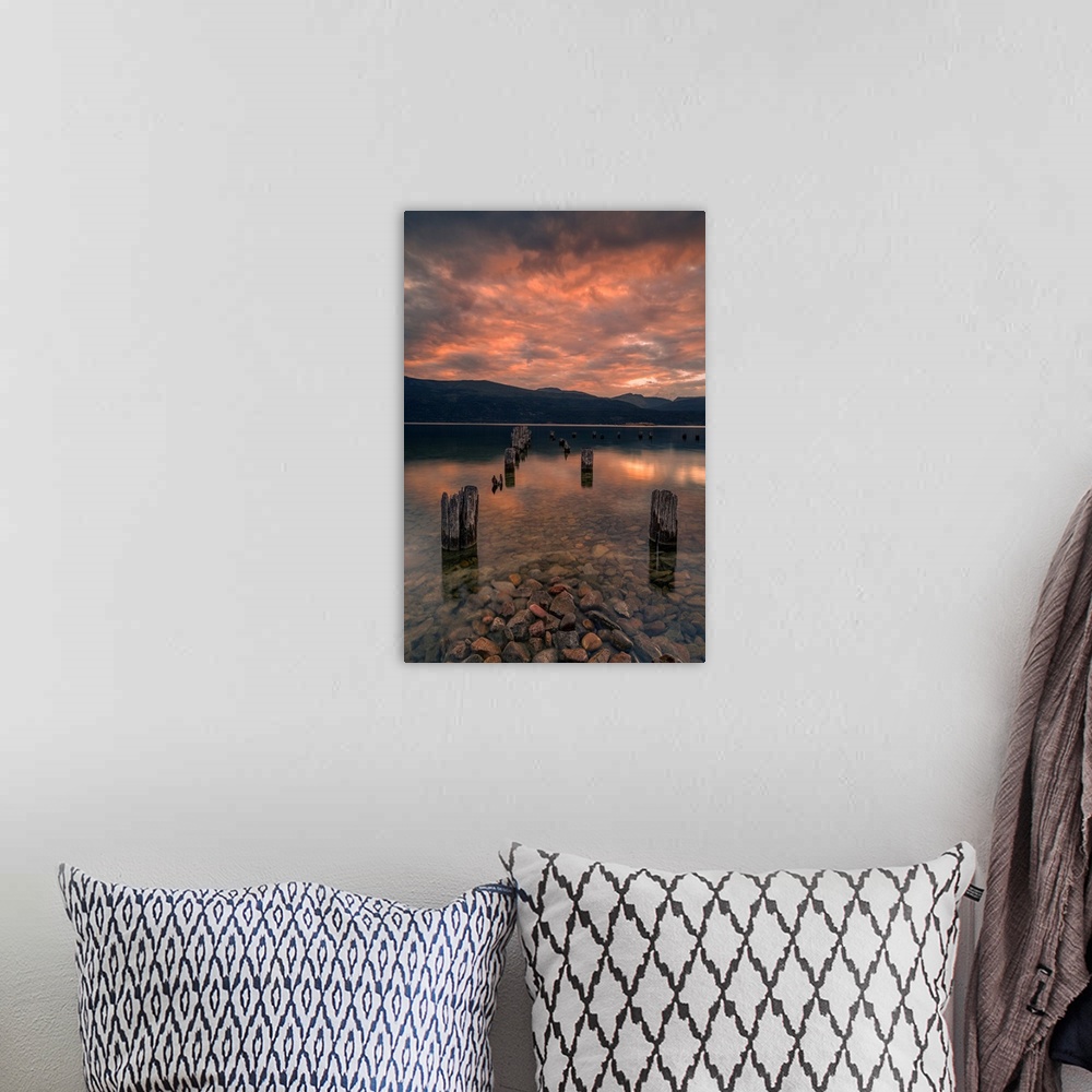 A bohemian room featuring Sunset on Okanagan Lake British Columbia, Canada overlooking abandoned dock pilings and lake rocks.