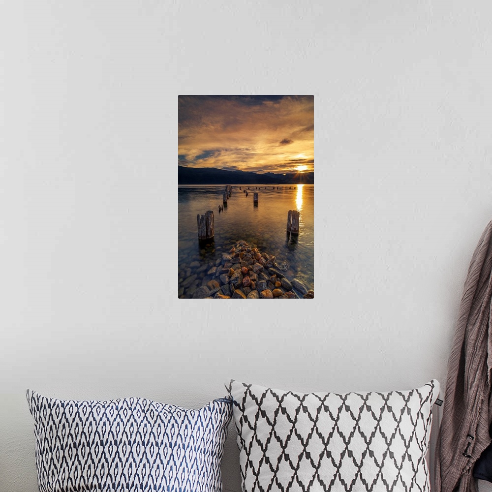 A bohemian room featuring Sunset on Okanagan Lake British Columbia, Canada overlooking abandoned dock pilings and lake rocks.