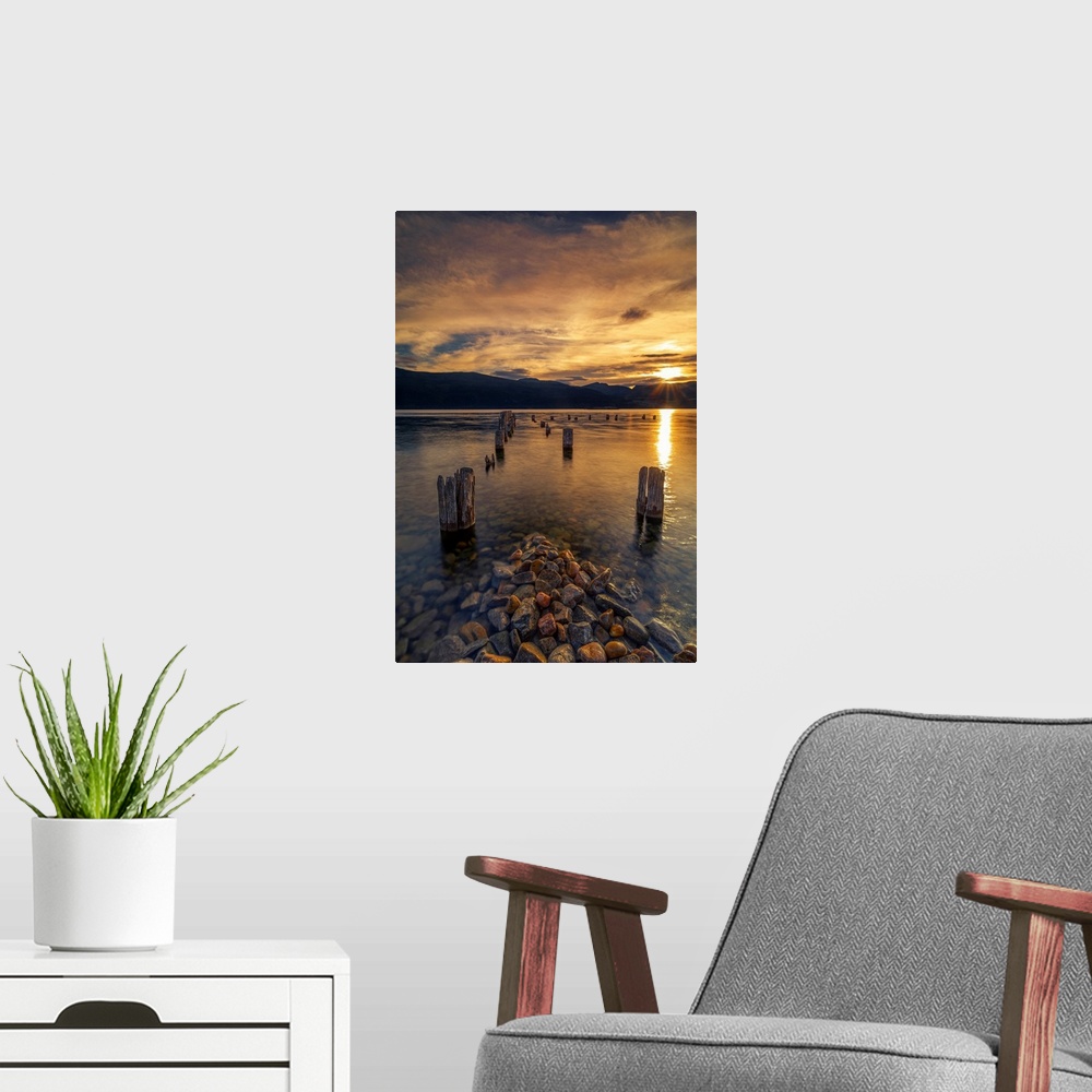 A modern room featuring Sunset on Okanagan Lake British Columbia, Canada overlooking abandoned dock pilings and lake rocks.
