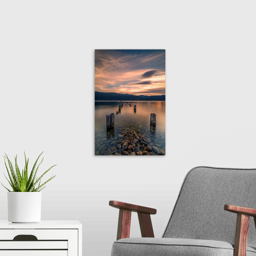 A modern room featuring Sunset on Okanagan Lake British Columbia, Canada overlooking abandoned dock pilings and lake rocks.