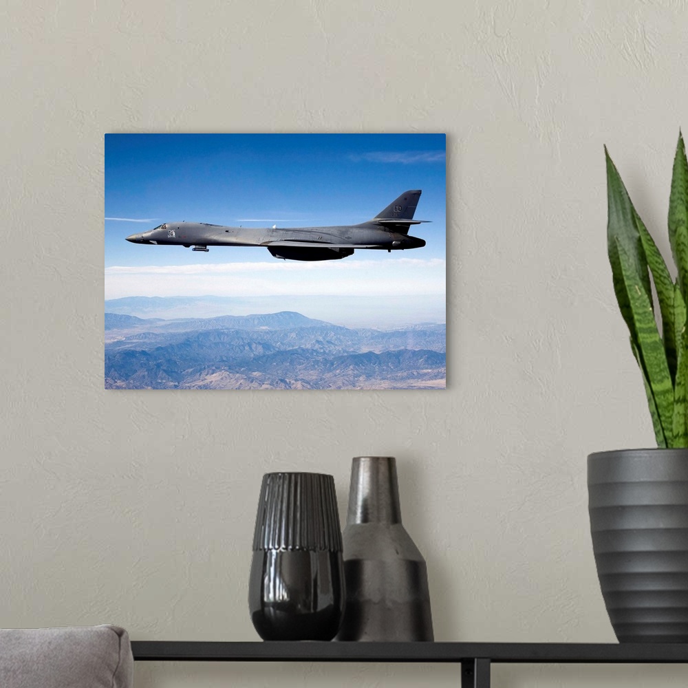 A modern room featuring A B-1B Lancer carries the Sniper pod on its belly as it flies through the sky.