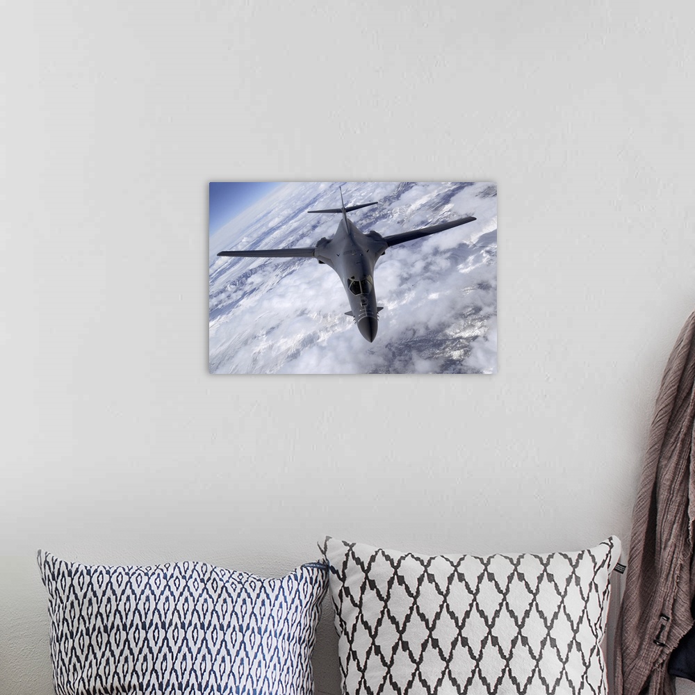 A bohemian room featuring A military aircraft is photographed flying above the clouds and over snowy mountainous terrain.