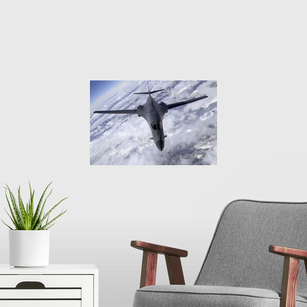 A modern room featuring A military aircraft is photographed flying above the clouds and over snowy mountainous terrain.