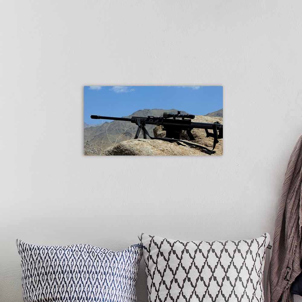 A bohemian room featuring Wall docor of a sniper rifle that is propped up on a stony ridge over looking mountains in Afghan...