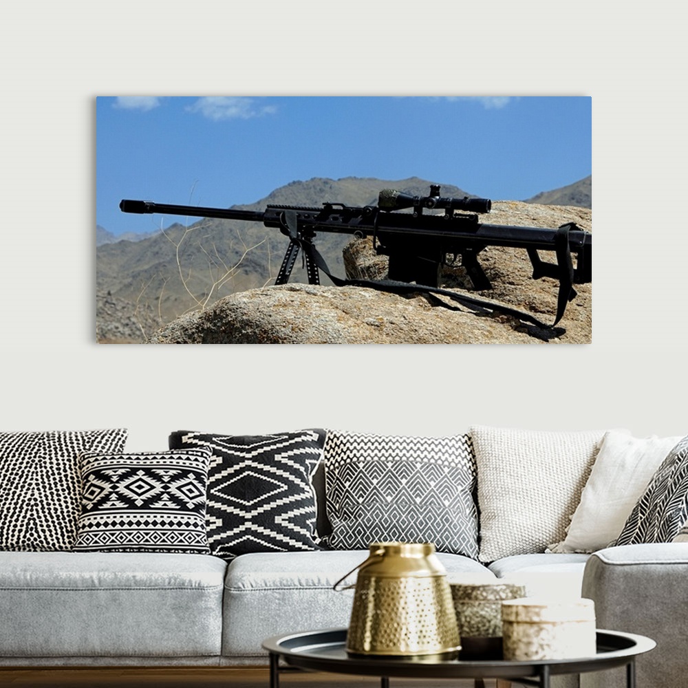 A bohemian room featuring Wall docor of a sniper rifle that is propped up on a stony ridge over looking mountains in Afghan...