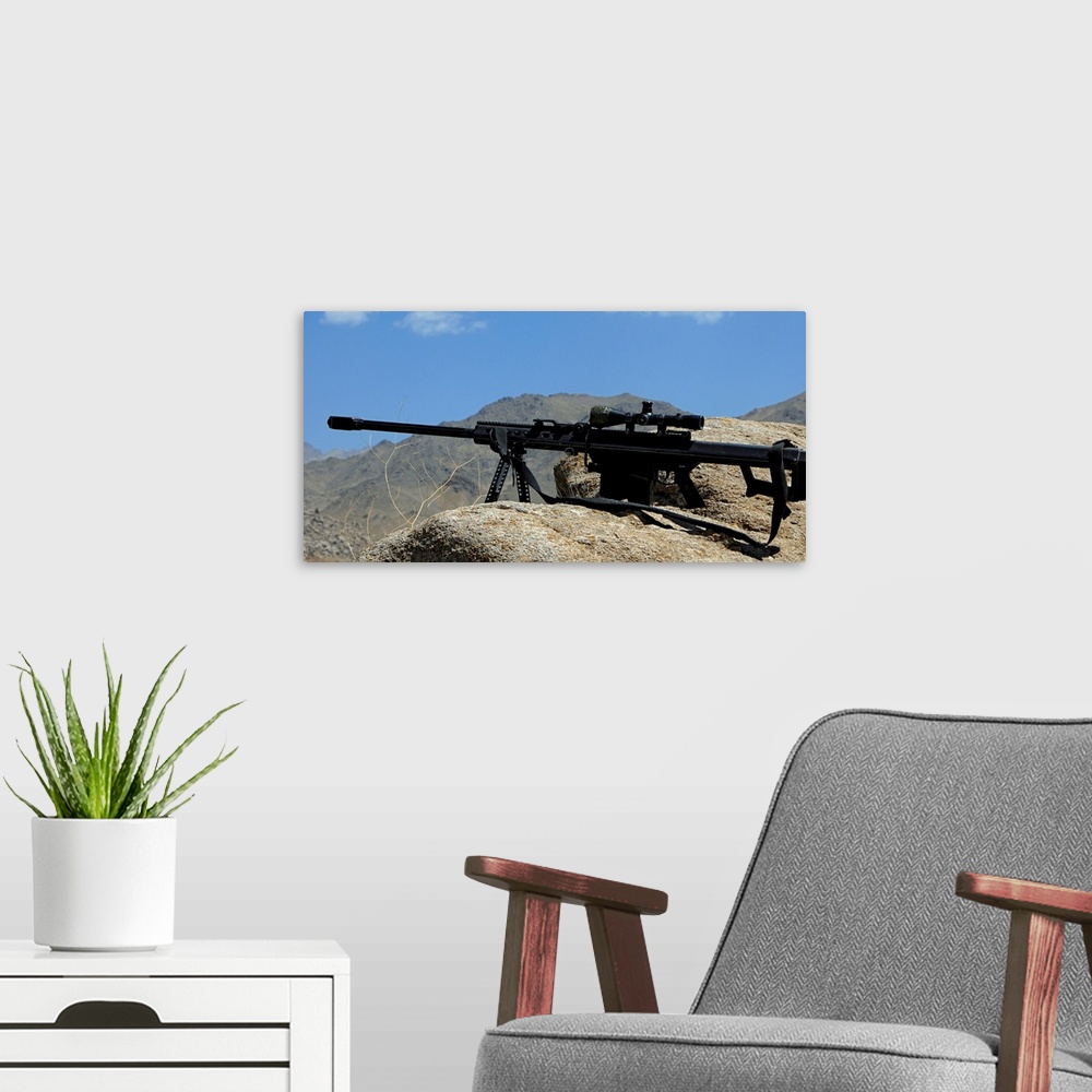 A modern room featuring Wall docor of a sniper rifle that is propped up on a stony ridge over looking mountains in Afghan...