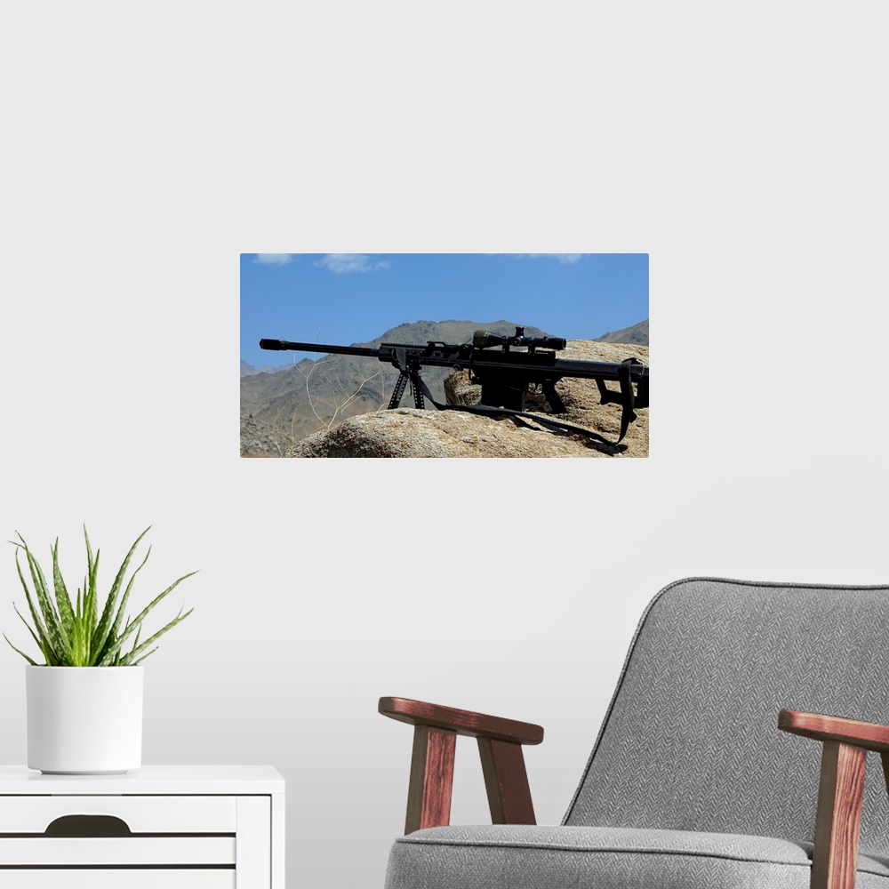 A modern room featuring Wall docor of a sniper rifle that is propped up on a stony ridge over looking mountains in Afghan...