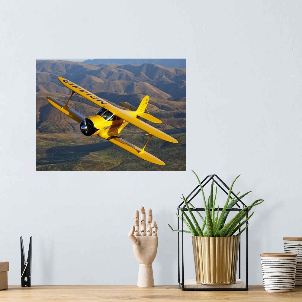 A bohemian room featuring Photograph of a Beechcraft D-17 Staggerwing single propeller biplane flying over rolling hills.